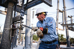 older man in safety gear and hard hat works on construction site and works with a wrench